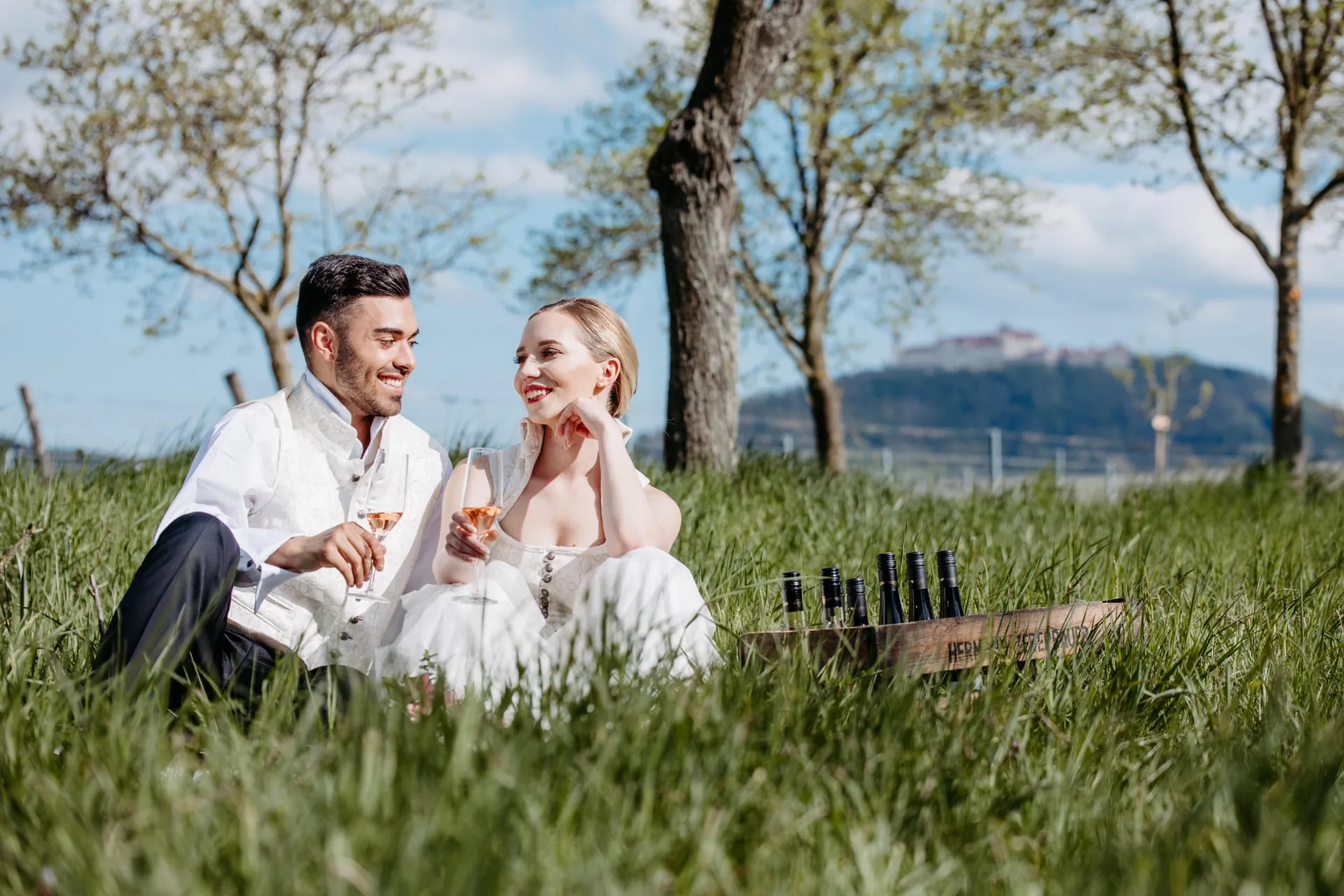 Brautpaar sitzt lachend im Gras mit Blick auf die Wachau – Hochzeitsfotografie von Alexander Pfeffel